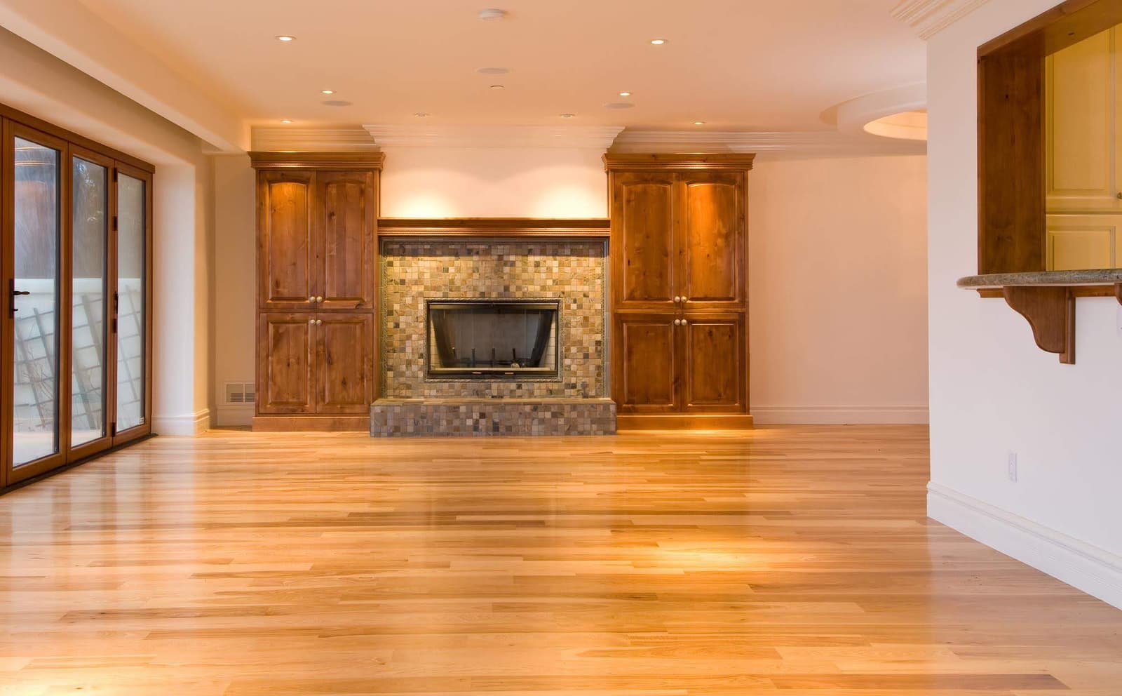 A spacious room with refinished hardwood flooring and wood cabinetry flanking a tiled fireplace, by Forever Flooring